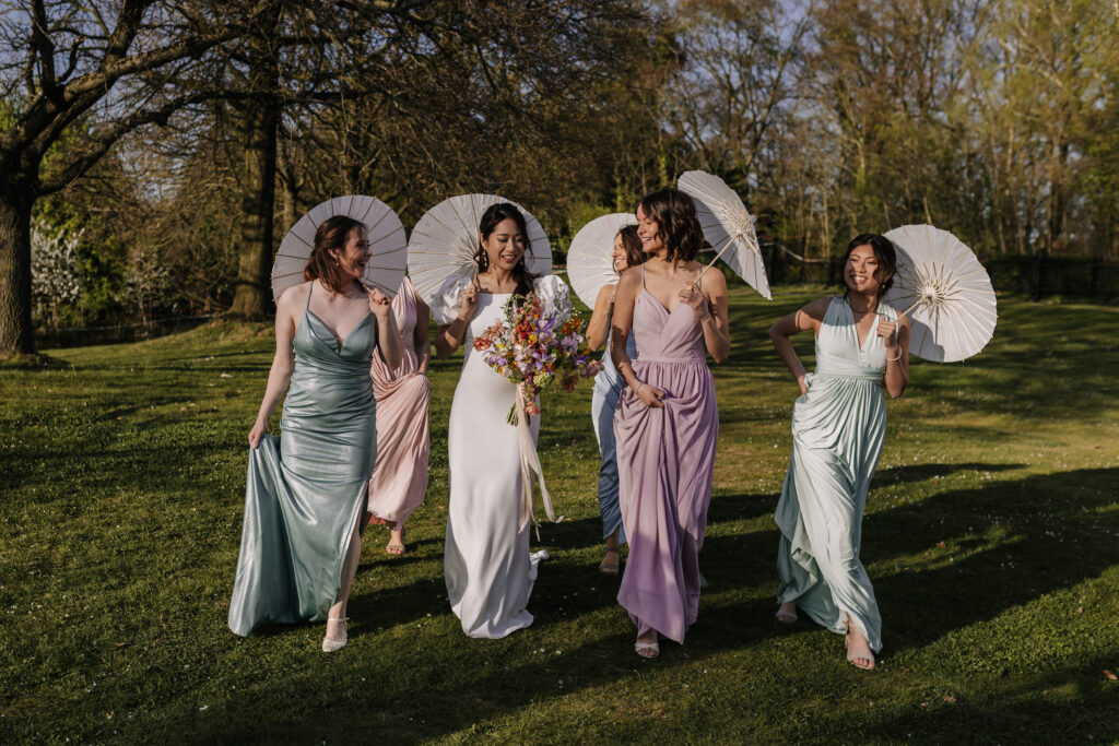 Veronika Rodriguez Hochzeitsplanerin für Mülheim an der Ruhr und Umgebung, Braut und Brautjungfern laufen über die Wiese mit Sonnenschirmchen in der Hand
